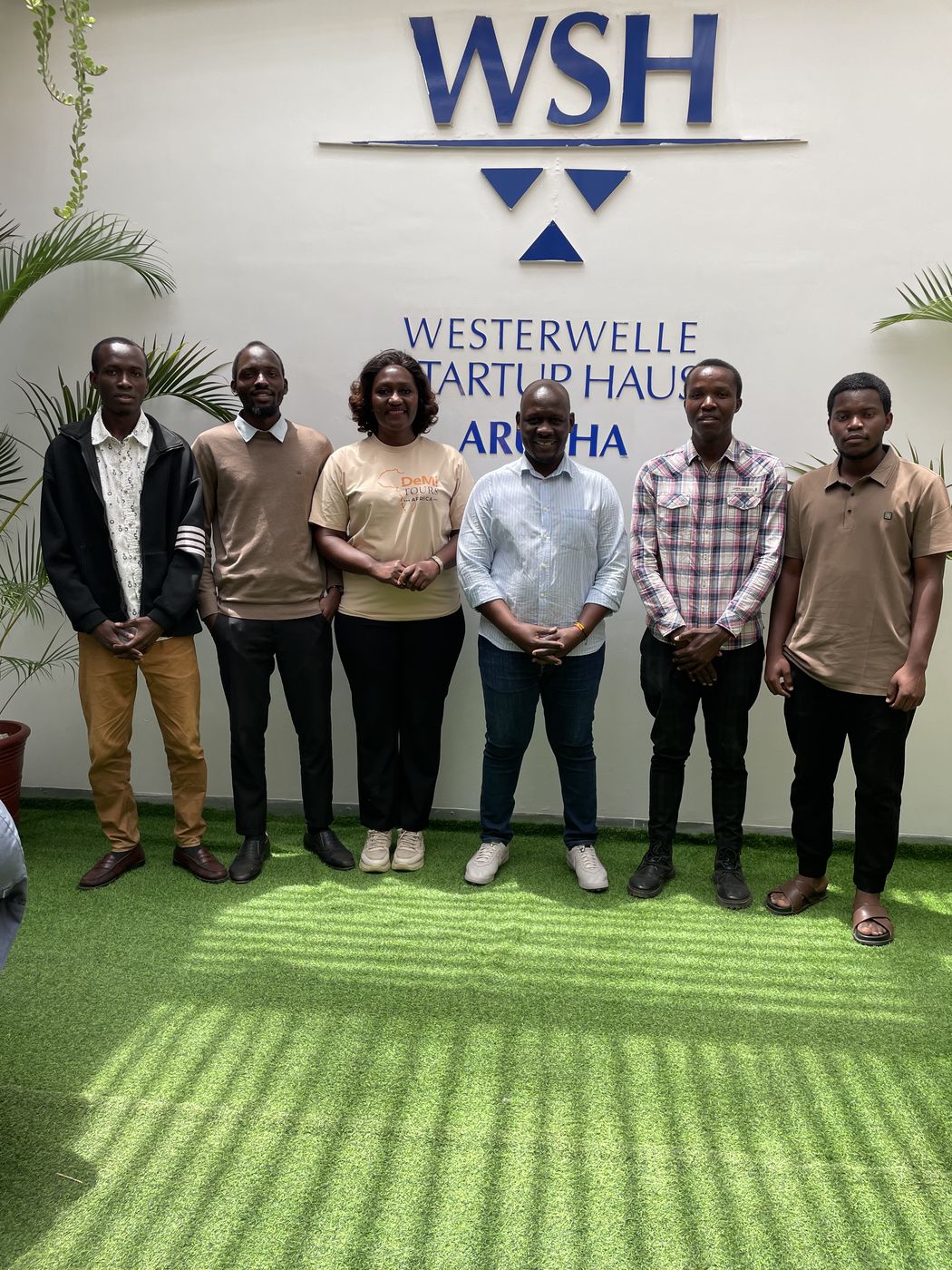 Founders and facilitator standing together under the Westerwelle Startup Haus Arusha sign